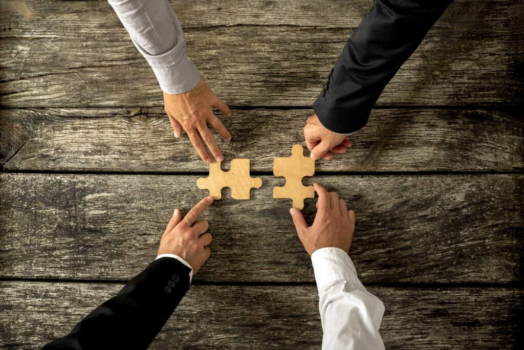 Four successful business men joining two puzzle pieces each being held by two partners, rustic wooden background. Conceptual of merger or creative cooperation of two business companies.